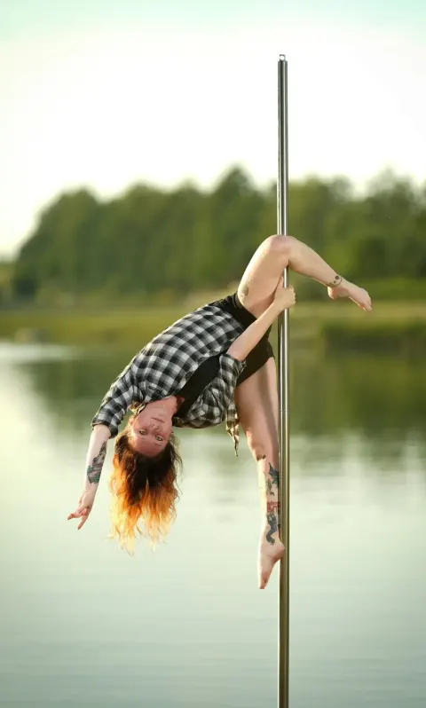 Pole dance – lektorka visí hlavou dolů na tyči a provádí efektní záklon ve studiu Prostě se hýbej, Opava.