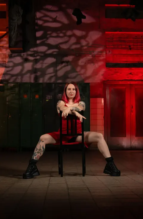 Chairdance – lektorka sedí na židli s rukama na opěradle a nohama široce rozkročenýma ve studiu Prostě se hýbej, Opava.