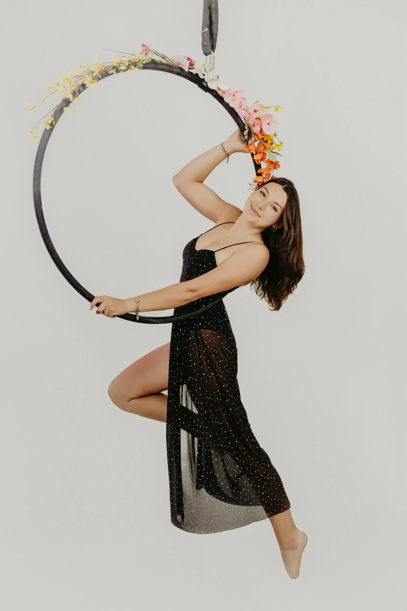 Aerial hoop – lektorka v elegantních šatech visí na květinami zdobeném kruhu a usmívá se ve studiu Prostě se hýbej, Opava.