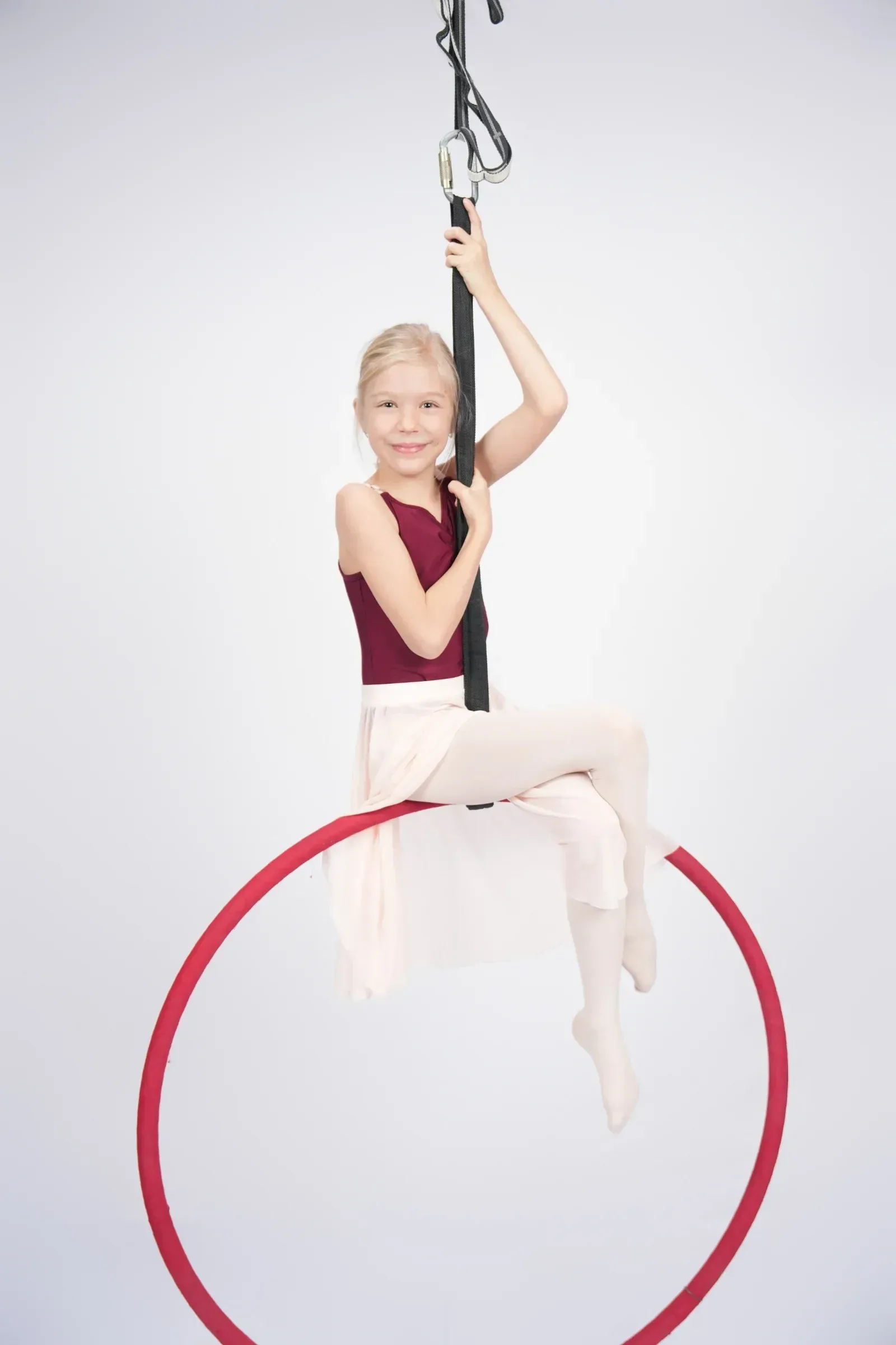 Hoop Kids – usměvavá holčička sedí na červeném aerial hoopu a drží se závěsu ve studiu Prostě se hýbej, Opava.