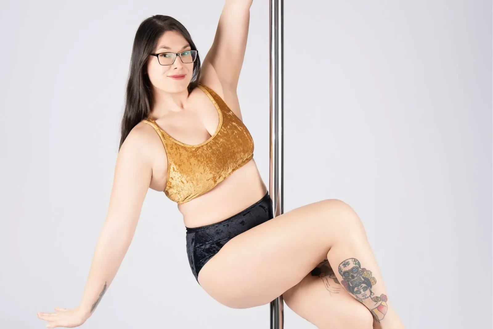 Pole dance – lektorka se drží tyče a usmívá se do objektivu v příjemné póze ve studiu Prostě se hýbej, Opava.